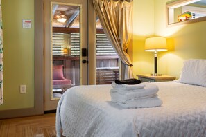 A hotel room with a bed, a nightstand with a lamp, a window with curtains, and a view of the outside. - Tranquil porch, Short walk to beach & CB Boardwalk (Carolina Beach)