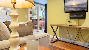 Un salon avec un canapé, une lampe, un téléviseur posé sur un meuble et un ordinateur portable sur une table.