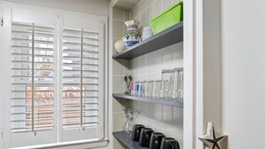Una cocina con paredes de azulejos blancos, una ventana con persianas, estantes con utensilios de cocina y un adorno con forma de estrella.