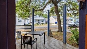 Un espacio de estar al aire libre cubierto con una mesa y sillas, un árbol grande y vistas de casas al fondo.
