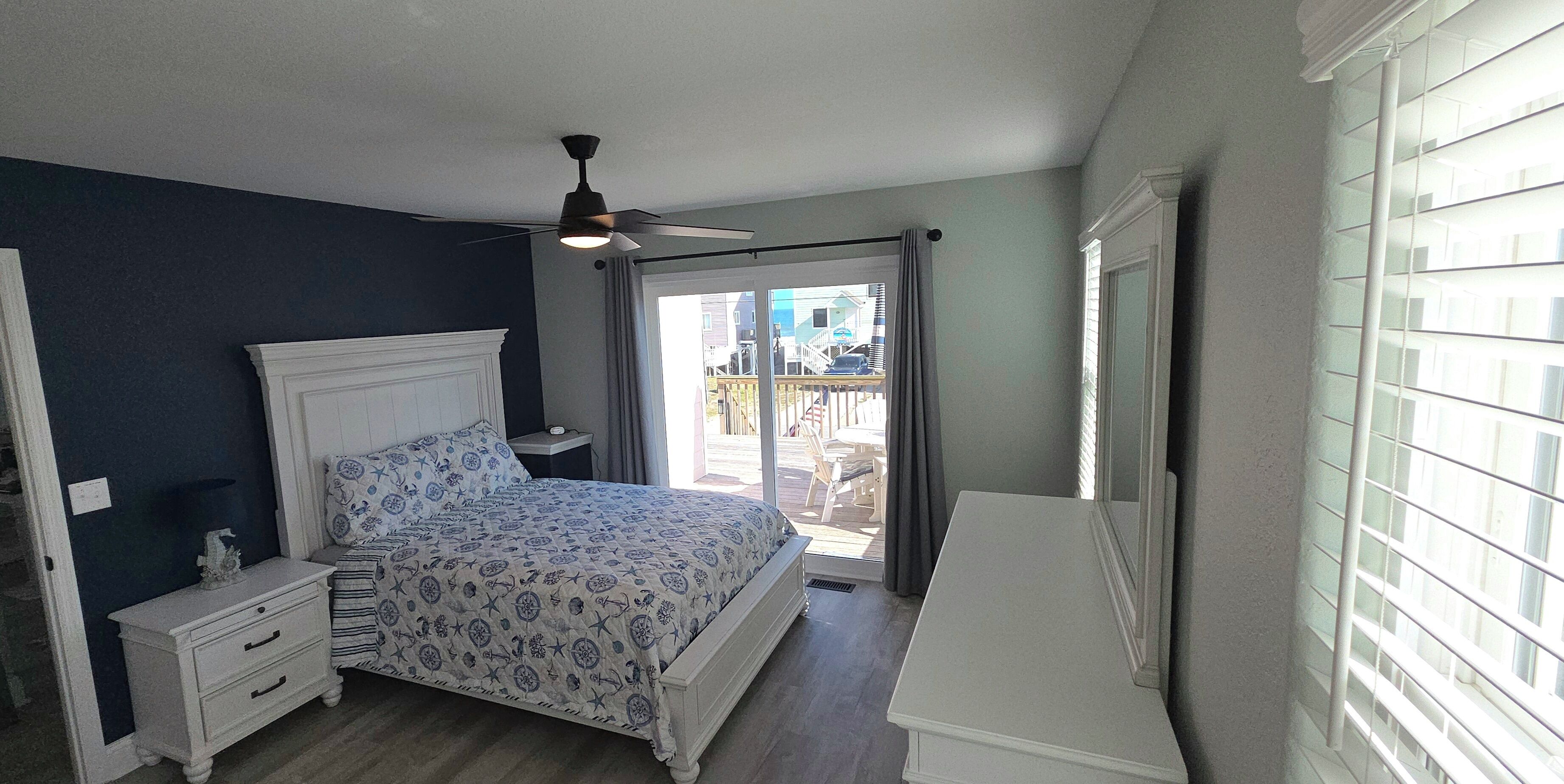 Une chambre à coucher comprenant un lit, une table de chevet, une commode, un ventilateur de plafond et une vue sur l’extérieur.