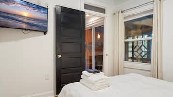 A bedroom with a bed, a TV on the wall, a door, and a window.