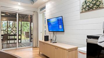 A modern room with a large flat-screen TV mounted on a white wall, a wooden cabinet, and a sliding glass door leading to an outdoor area.
