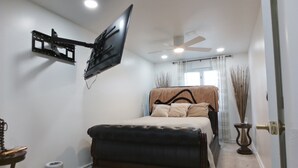 Camera da letto con un letto, una TV a parete, una ventola a soffitto e una porta con pomello decorativo.