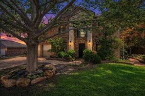 Une maison en briques avec un grand arbre dans le jardin, un garage et une pelouse bien entretenue.