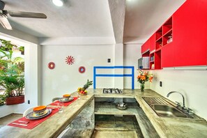 Eine Küche mit Kochinsel, Spüle und Herd. Es sind Wandverzierungen und ein rotes Schranksystem vorhanden.