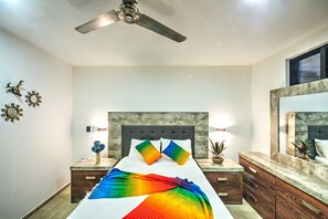 Ein Schlafzimmer mit einem Bett, einem Deckenventilator, einem Nachttisch mit Lampe, einem Spiegel und Wanddekoration.