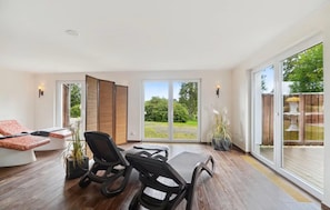 A spacious room with a large sliding glass door leading to a garden, a dining table with chairs, and a sofa with cushions. - Ferienhaus am Hotel mit Gastro und Wellnes (Oberharz am Brocken)