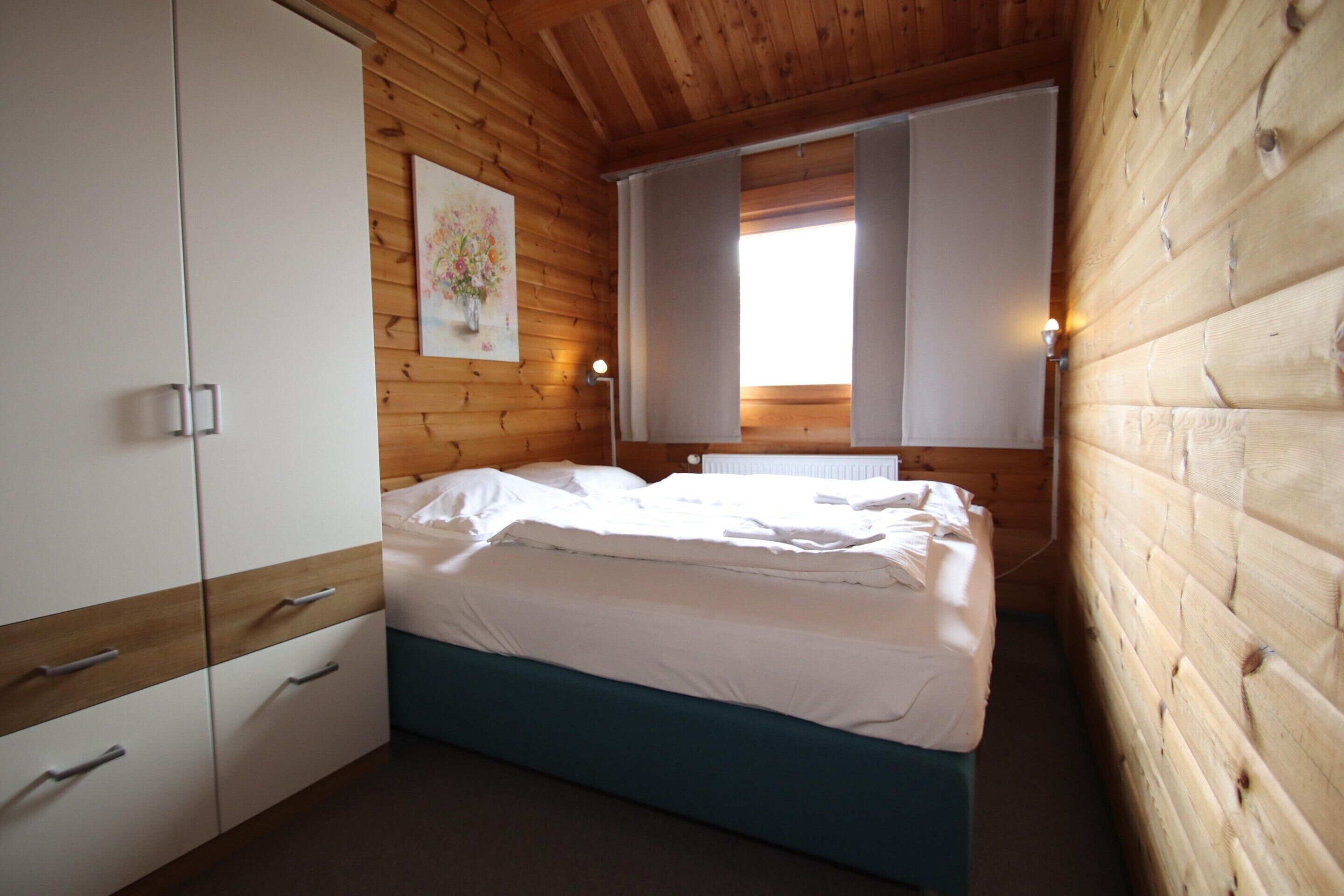 Une chambre à coucher avec un lit, des murs en bois, une armoire blanche et un tableau accroché au mur.