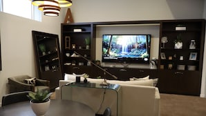 A modern living room with a flat-screen TV, a glass coffee table, a sofa, and built-in shelving with decorative items.