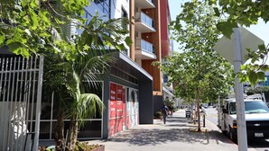 A modern building with balconies, a sidewalk, and a parked vehicle.