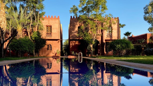 Ein spiegelnder Pool vor einer symmetrischen Gebäudefassade mit Rundbogenfenstern und einem zentralen Eingang.