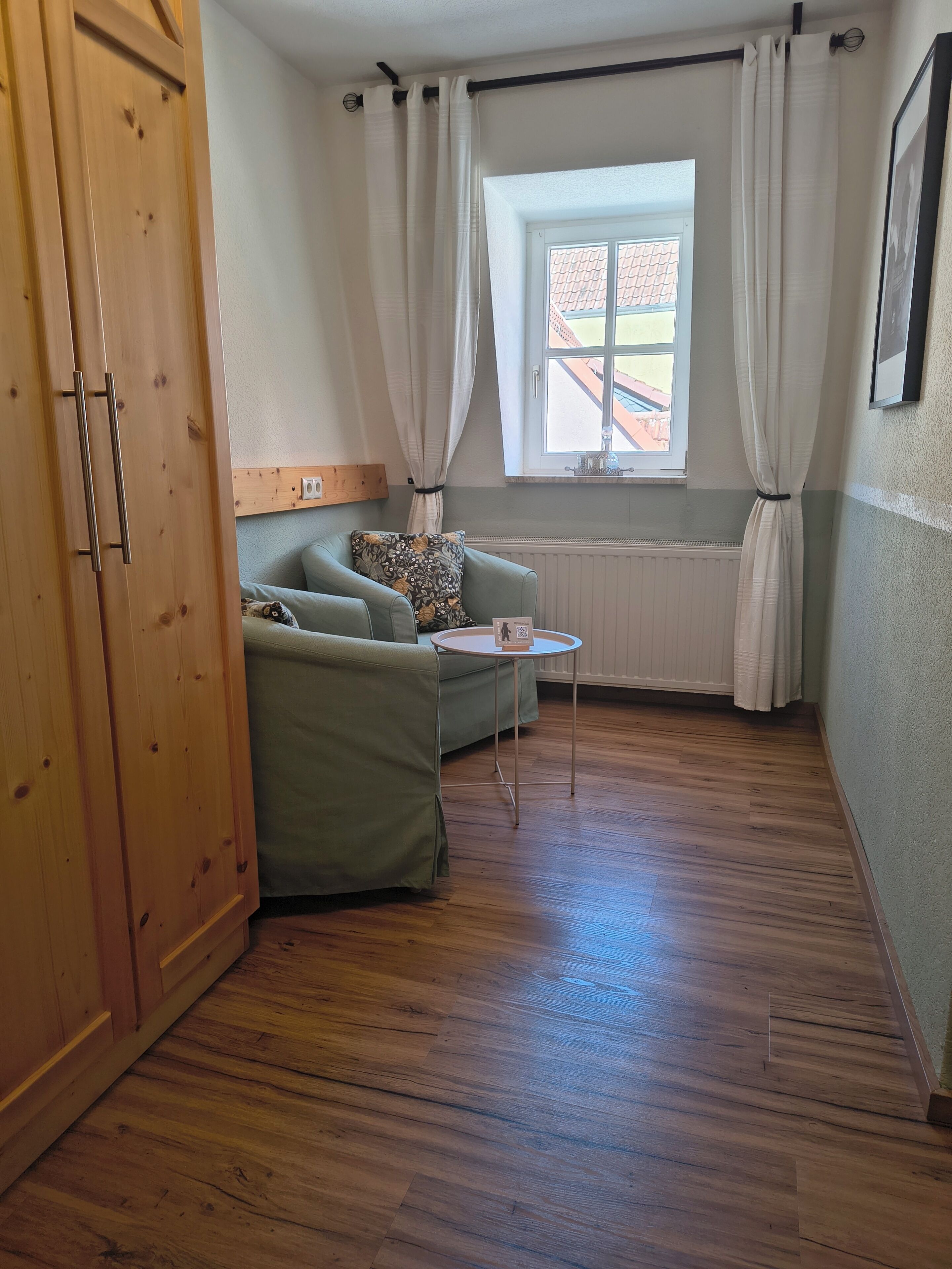 Una habitació amb un armari de fusta, un sofà verd, una taula rodona petita i una finestra amb cortines.