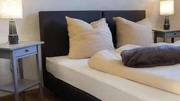 A neatly made bed with pillows and a blanket, a bedside table with a lamp, and a small rug on the floor.