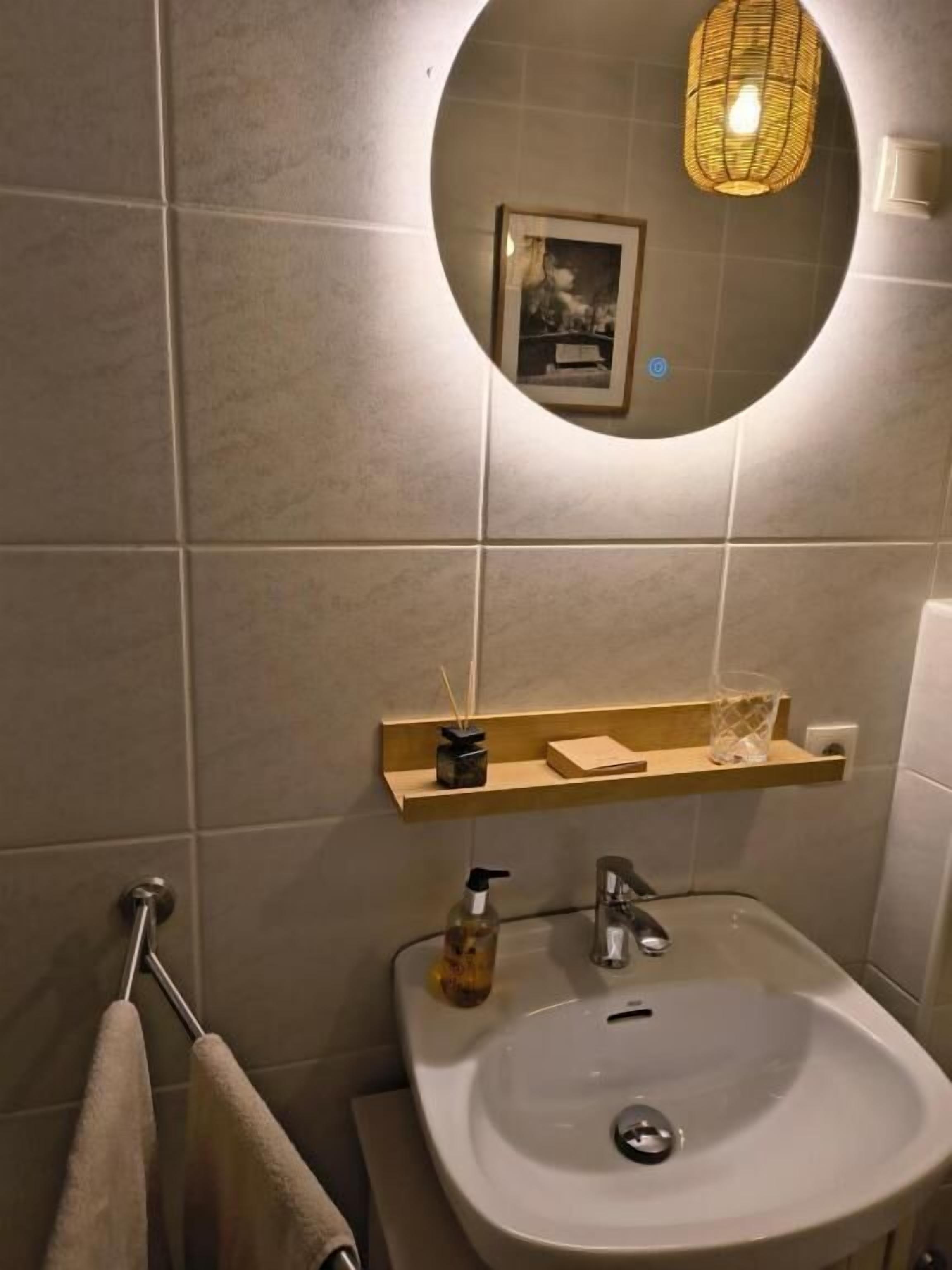 A bathroom with a round mirror, a sink, a towel rack, and a shelf with toiletries.