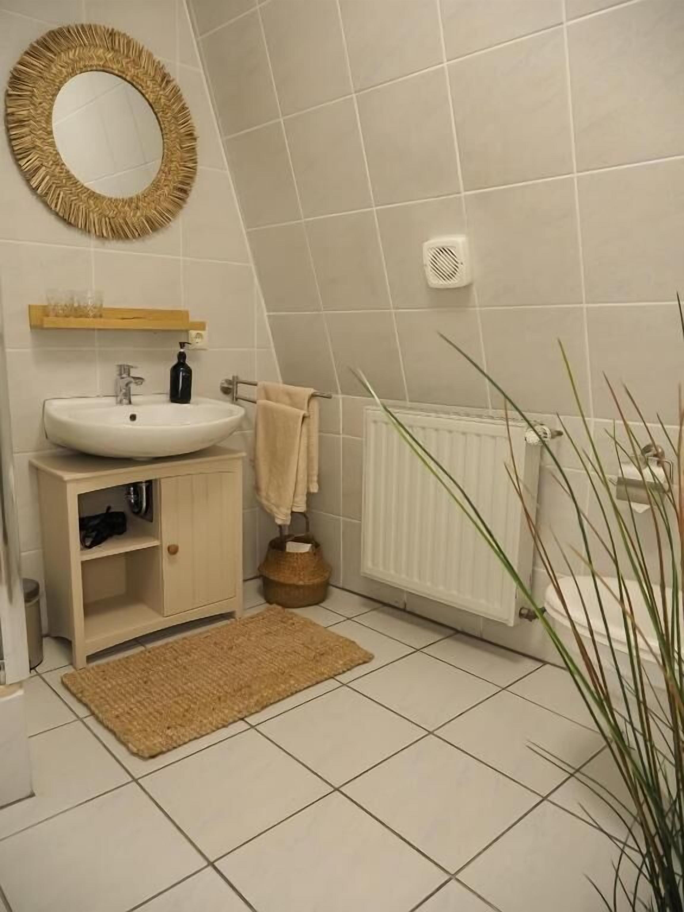 A bathroom with a round mirror, a sink, a wooden cabinet, a towel rack, a radiator, and a plant.