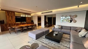 Ein modernes Wohnzimmer mit Sofa, Hocker, Couchtisch und einem Essbereich mit Stühlen und einem Holztisch.