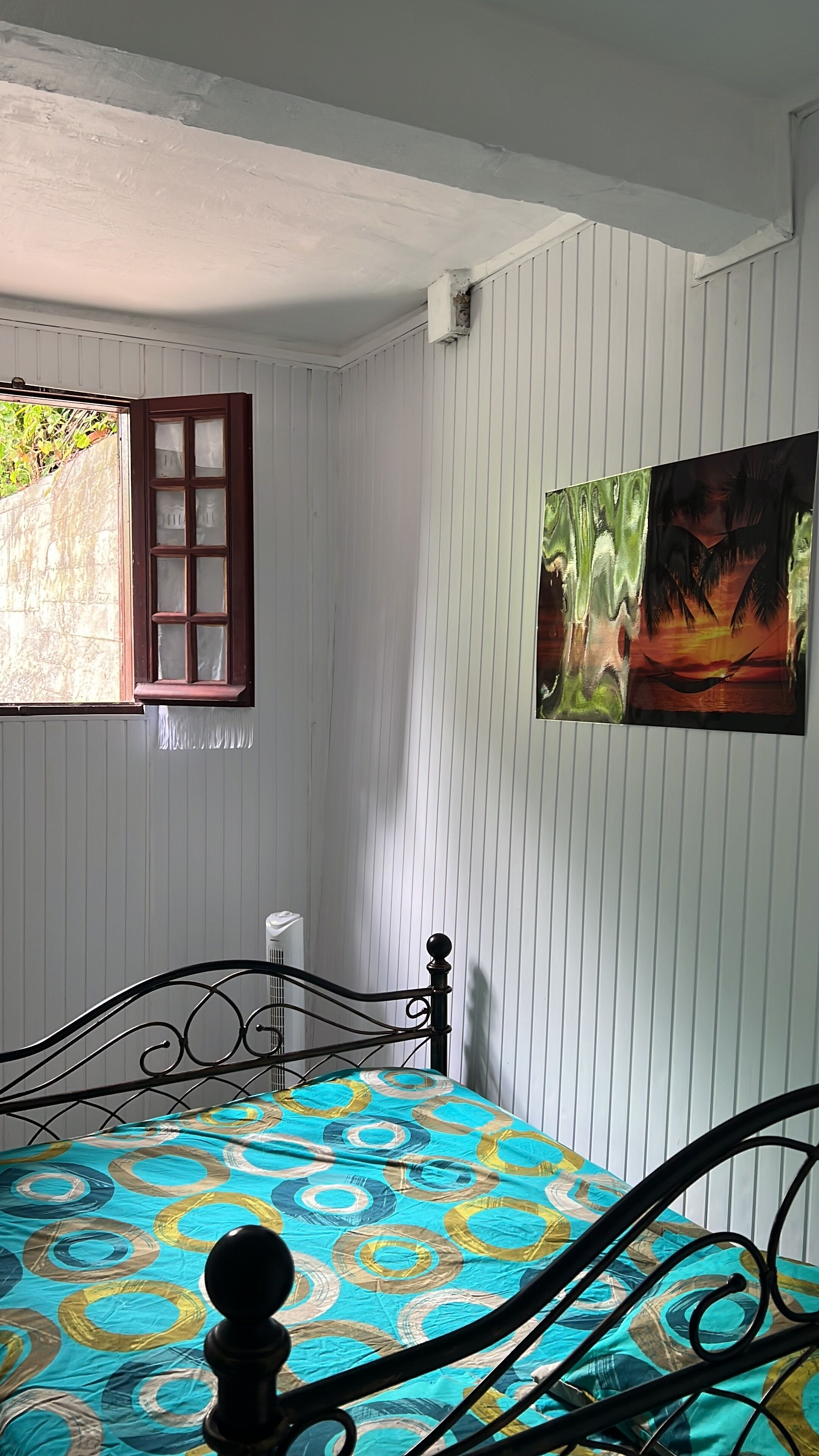 Une pièce avec un lit, une fenêtre à cadre en bois et un tableau accroché au mur.