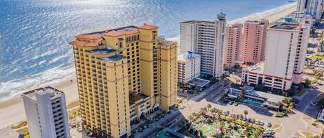 A coastal hotel with multiple high-rise buildings, a parking area, and a beach view.