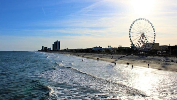 Ein Strand mit einem großen Riesenrad, Meereswellen und blauem Himmel.
