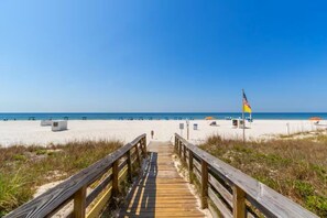 A wooden boardwalk leading to a beach with a flag, clear skies, and a sandy shore. - Gulf front beautiful beachfront great view large balcony 2 king beds Royal Palms (Gulf Shores)