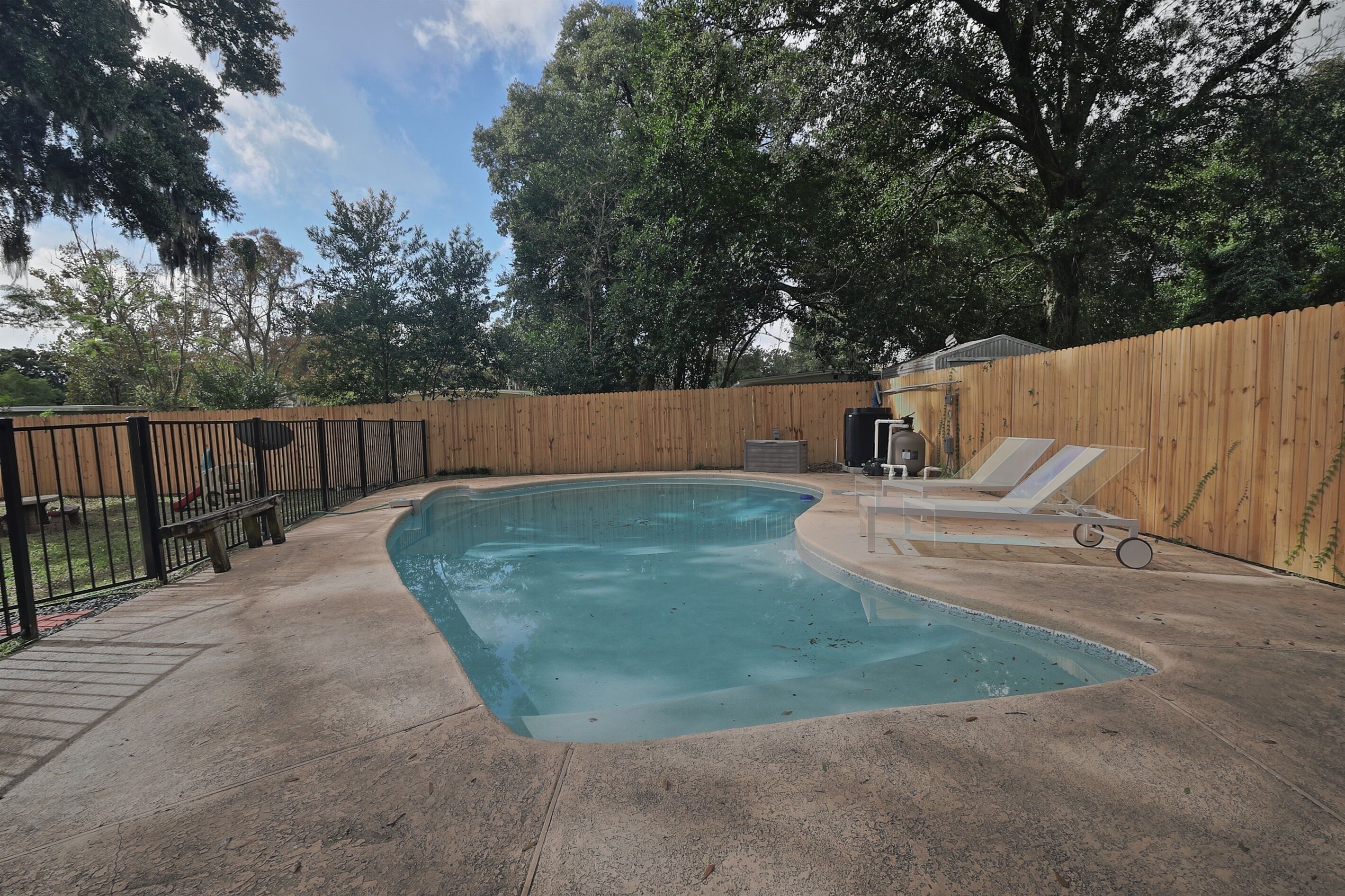 Un patio trasero con piscina, cerca de madera y banco.