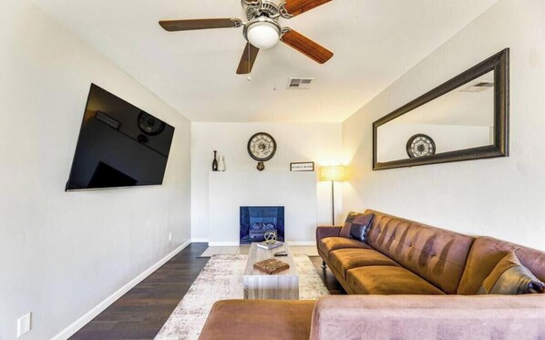 A living room with a ceiling fan, a fireplace, a sofa, a coffee table, and a mirror on the wall. - Desert Oasis with Private Pool & Backyard Fun (Tempe)