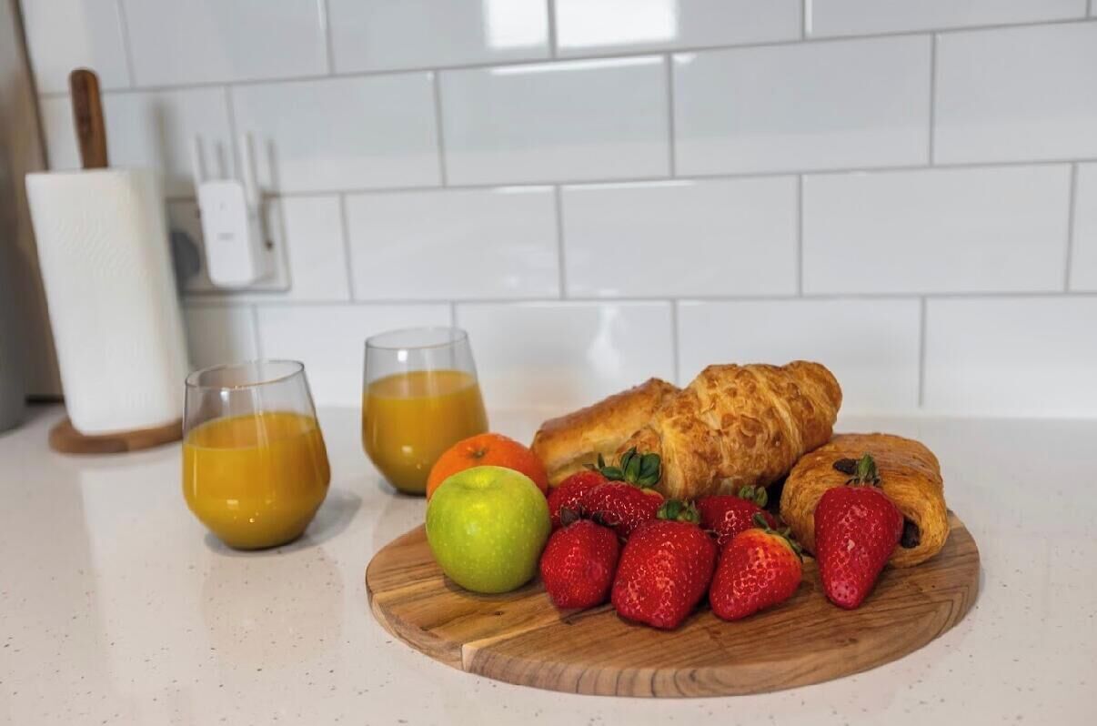 En morgenmadsanretning med kager, jordbær, et æble og to glas appelsinjuice på en træplade.