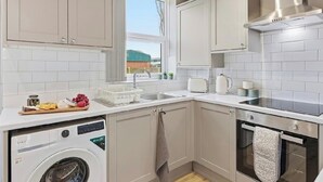 A compact kitchen with a washing machine, a sink, a stove, and a window. - Modern 3BR | Parking | Work trips | Relocators | Events | Flexible stays (Manchester)