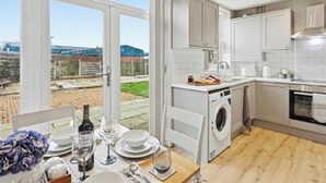 A modern kitchen with a washing machine, a dining area with a table set for two, and a view of the outside. - Modern 3BR | Parking | Work trips | Relocators | Events | Flexible stays (Manchester)