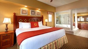 Habitación de hotel con una cama grande, dos lámparas de noche, un ventilador de techo, un baño con bañera y vistas a la cocina.