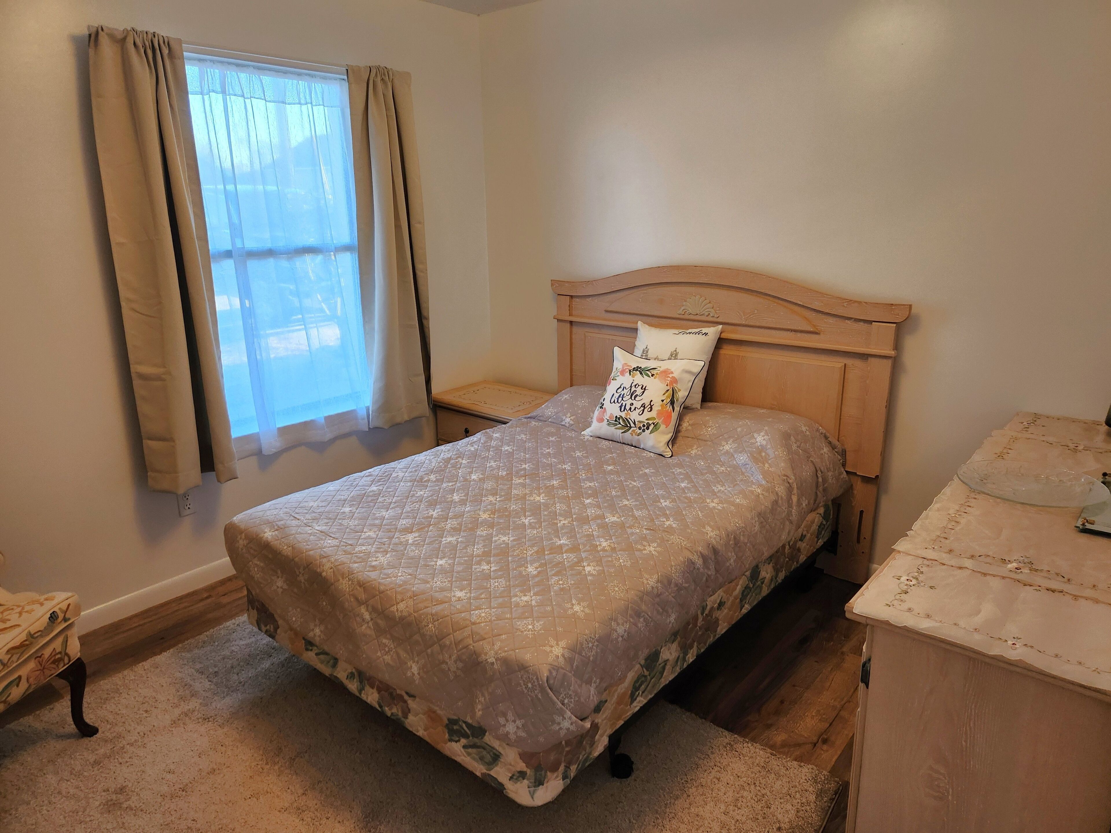 A bedroom with a bed, a nightstand, a dresser, a window with curtains, and a carpeted floor.