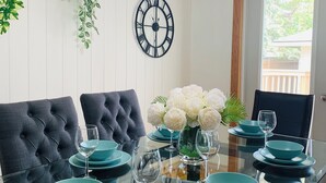 Een eettafel met turquoise borden en glazen, zwarte gestoffeerde stoelen, een wandklok en een hanglamp.