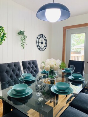 Une table à manger avec des assiettes et des verres de couleur turquoise, des chaises à revêtement noir, une horloge murale et un luminaire suspendu.