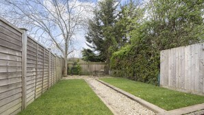 A backyard with a wooden fence, a gravel path, and a grassy area. - Stylish 2-Bed Home Close to Cheltenham Town Centre (Cheltenham)