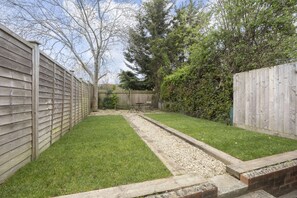 A backyard with a wooden fence, a gravel path, and a grassy area. - Stylish 2-Bed Home Close to Cheltenham Town Centre (Cheltenham)