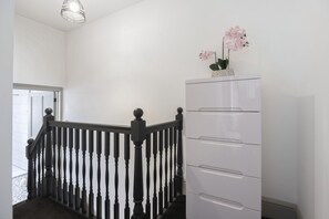 Eine Treppe mit schwarzer Geländer, eine weiße Kommode mit Schubladen und eine Vase mit rosa Blumen darauf.