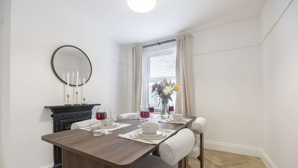 A dining room with a wooden table set for four, a fireplace, and a large mirror on the wall. - Stylish 2-Bed Home Close to Cheltenham Town Centre (Cheltenham)
