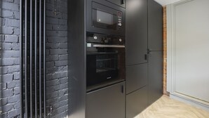 A kitchen with a microwave, oven, and built-in refrigerator, adjacent to a brick wall and a white door. - Stylish 2-Bed Home Close to Cheltenham Town Centre (Cheltenham)