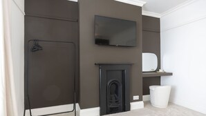 A room with a fireplace, a television mounted on the wall, and a white trash bin. - Stylish 2-Bed Home Close to Cheltenham Town Centre (Cheltenham)