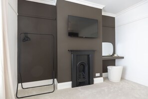 A room with a fireplace, a television mounted on the wall, and a white trash bin. - Stylish 2-Bed Home Close to Cheltenham Town Centre (Cheltenham)