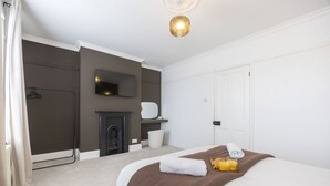 A bedroom with a bed, a fireplace, a TV, and a door. - Stylish 2-Bed Home Close to Cheltenham Town Centre (Cheltenham)