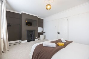 A bedroom with a bed, a fireplace, a TV, and a door. - Stylish 2-Bed Home Close to Cheltenham Town Centre (Cheltenham)