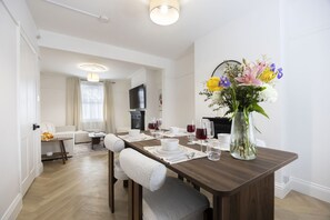 Ein Essbereich mit einem Holztisch, gedeckt für vier Personen, einer Blumenvase und einem Fernseher im Hintergrund.