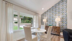 Una habitación con una mesa de comedor, sillas, un sofá, un papel tapiz estampado y vistas a través de una ventana.