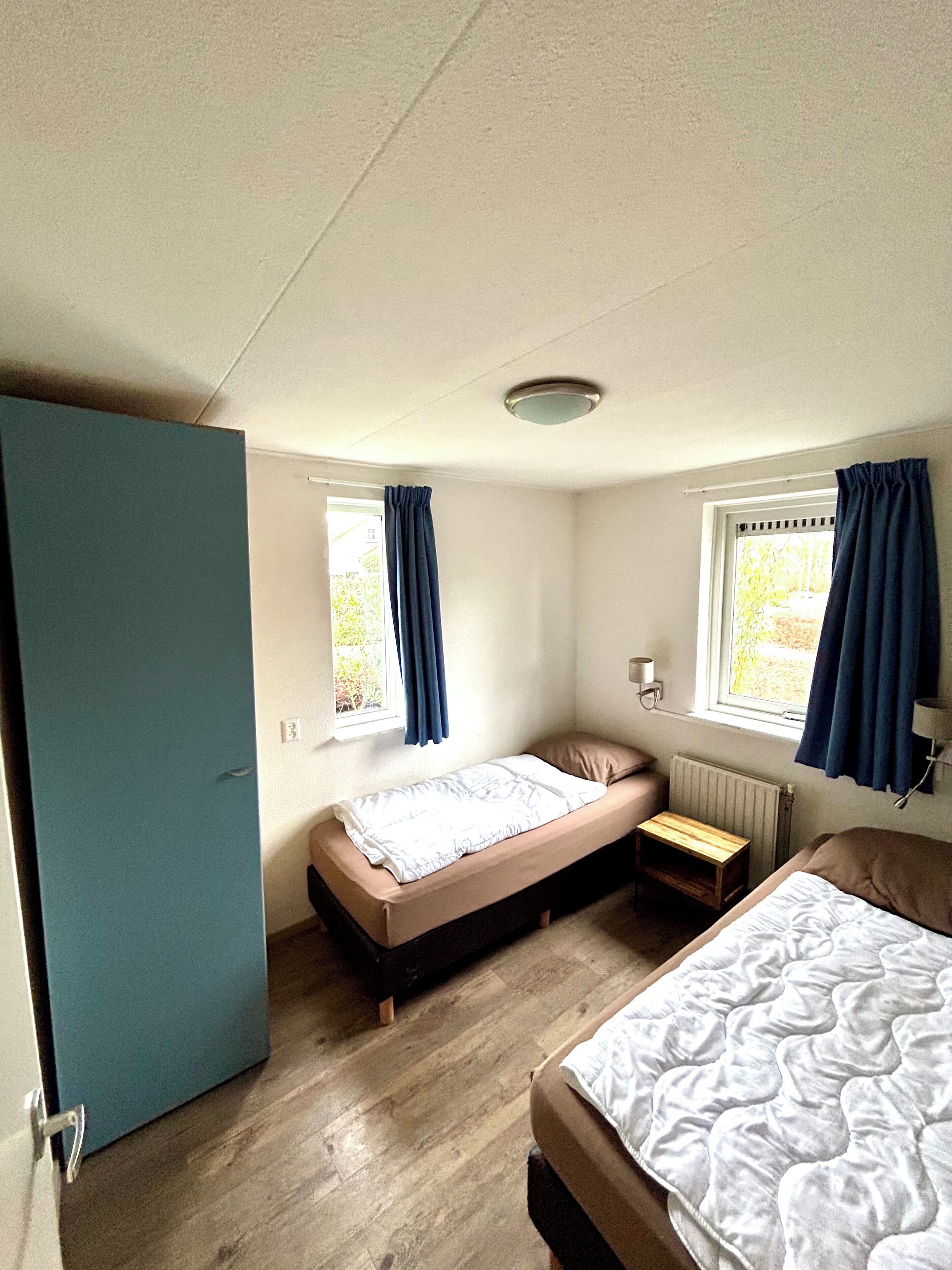 A small, single-room accommodation with a bed, a small table, and a window with curtains.