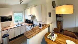 Eine moderne Küche mit weißen Schränken, einer Holzausziehtafel, einem eingebauten Ofen und einem Essbereich mit Tisch und Stühlen.