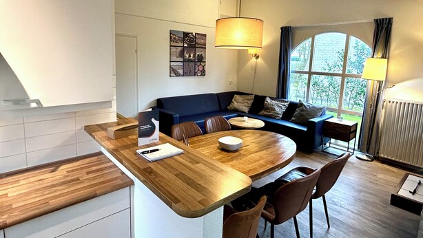 Eine moderne Küche mit einer Holzinsel, einem Essbereich mit rundem Tisch und einer Sitzecke mit Sofa und Sesseln.