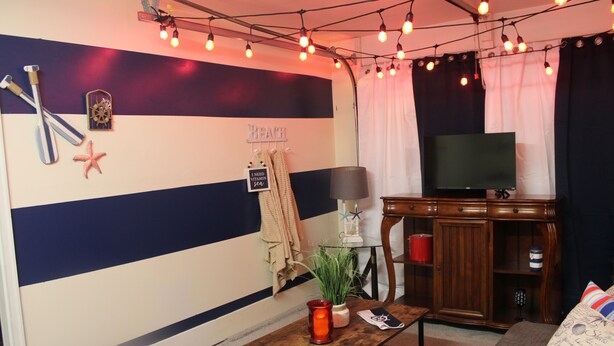 Quarto com parede listrada, televisão, armário de madeira, pequena mesa com vela e luzes de Natal.