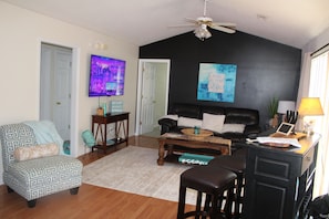 Un salon avec un mur noir, un ventilateur de plafond, un téléviseur, un canapé, une table basse et un bureau avec une lampe.